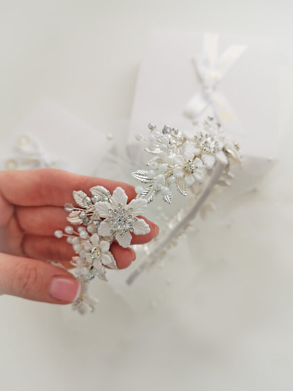 Moderna kruna za vjenčanje, nosi se poput rajfa za kosu. Uzrađena je od bijelih cvjetova i metalnih srebrnih listića, dodatno ukrašena sa Swarovski perlicama.