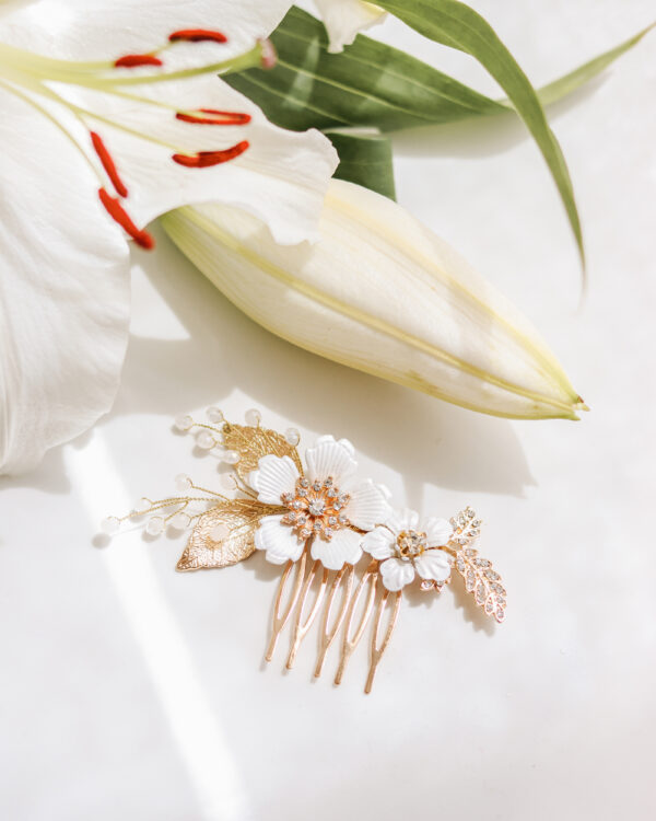 Češljić za kosu u bijelim i zlatnim tonovima. Izrađen od bijelih cvjetova upotpunjen zlatnim listićima, cirkonima i Swarovski perlicama.